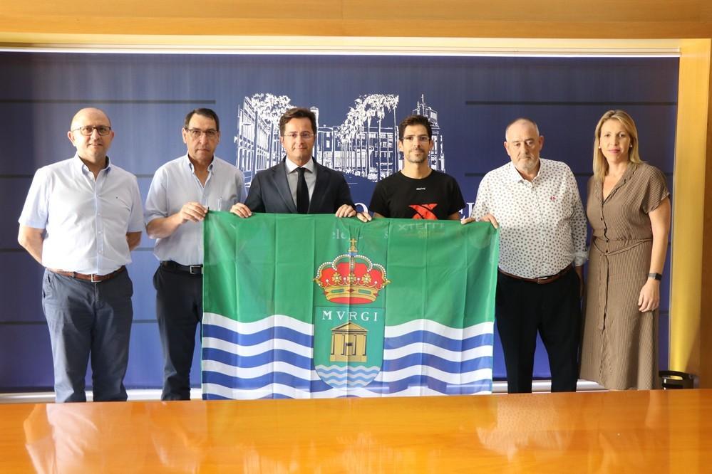 El alcalde entrega la bandera del municipio a Bernardo Rubio ante su próxima participación en el mundial de triatlón en Hawai